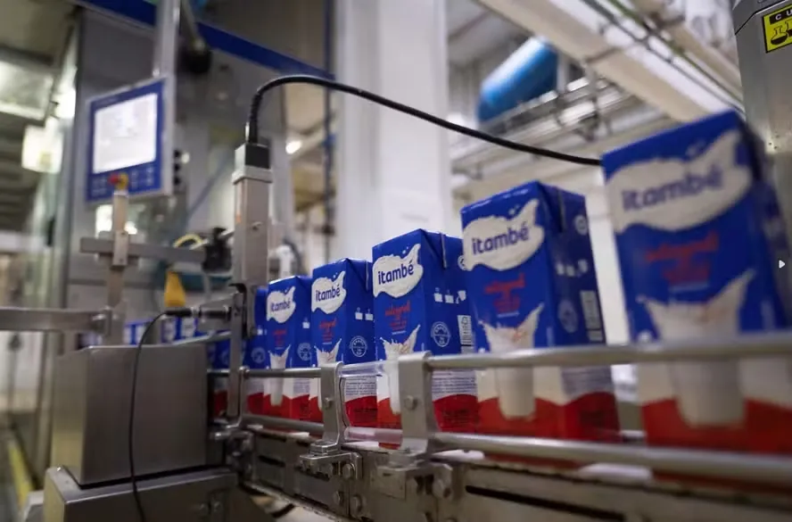 Caixas de leite Itambé em uma linha de produção industrial automatizada, representando a operação otimizada pelo planejamento integrado da cadeia de suprimentos.