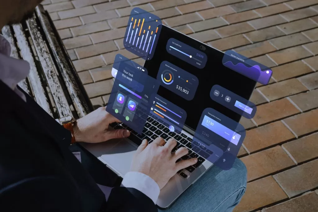 Close-up de mãos digitando em um laptop com visualizações digitais de gráficos e dashboards flutuando ao redor, representando a análise de dados digital e a flexibilidade de trabalhar com data analytics em qualquer lugar.