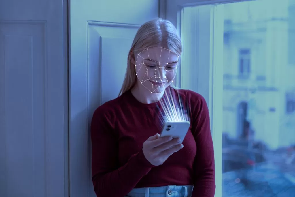  Uma pessoa interagindo com um smartphone que utiliza reconhecimento facial, mostrando uma interface comum onde a Inteligência Artificial facilita a interação entre humanos e máquinas no dia a dia.