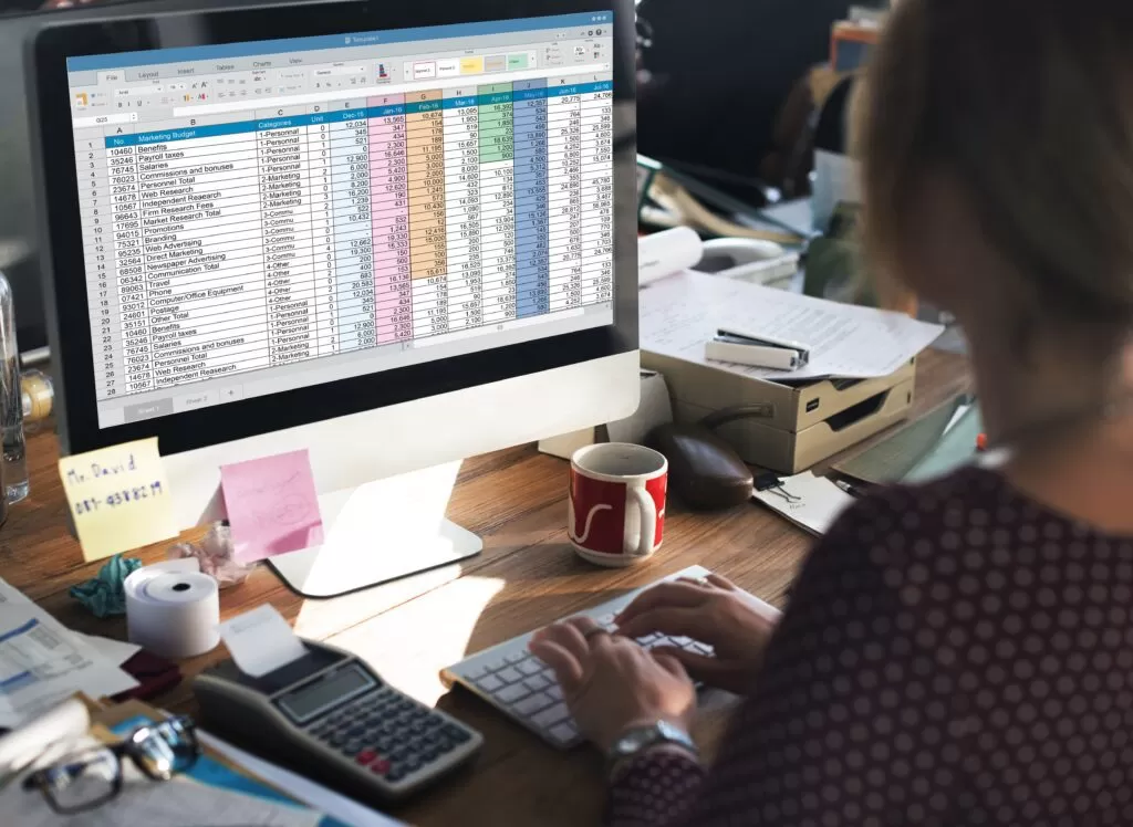 Pessoa trabalhando em uma planilha eletrônica em um computador, representando o uso inicial do Excel para análise de dados no planejamento acadêmico.