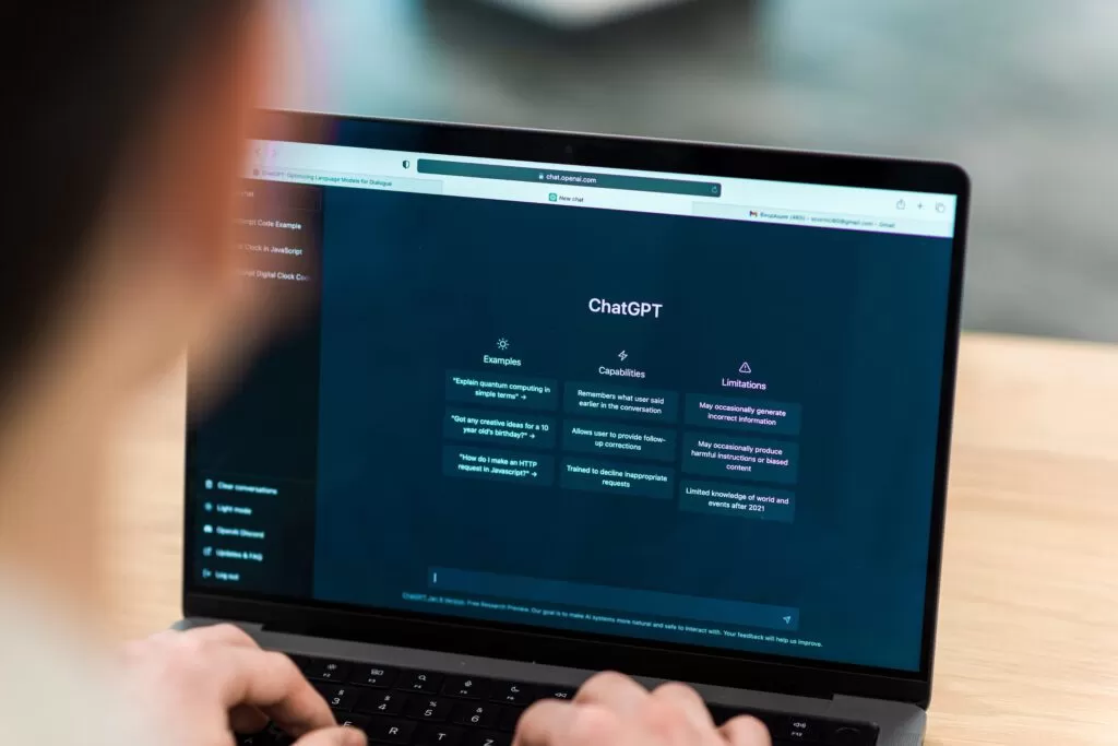 Mãos digitando em um laptop com a página inicial do ChatGPT visível na tela, representando a interação do usuário com a ferramenta de Inteligência Artificial para obter respostas e informações.