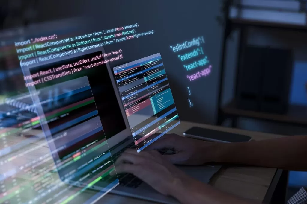 Mãos digitando em um laptop com código de programação e elementos de interface de usuário sobrepostos, representando o processo de desenvolvimento de software e a criação de uma ferramenta customizada para o planejamento da produção da Alpargatas.