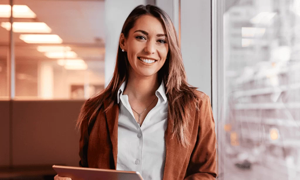 Uma profissional sorridente segurando um tablet, representando a aplicação prática das ferramentas de pesquisa operacional em um ambiente empresarial moderno para otimizar decisões e processos.