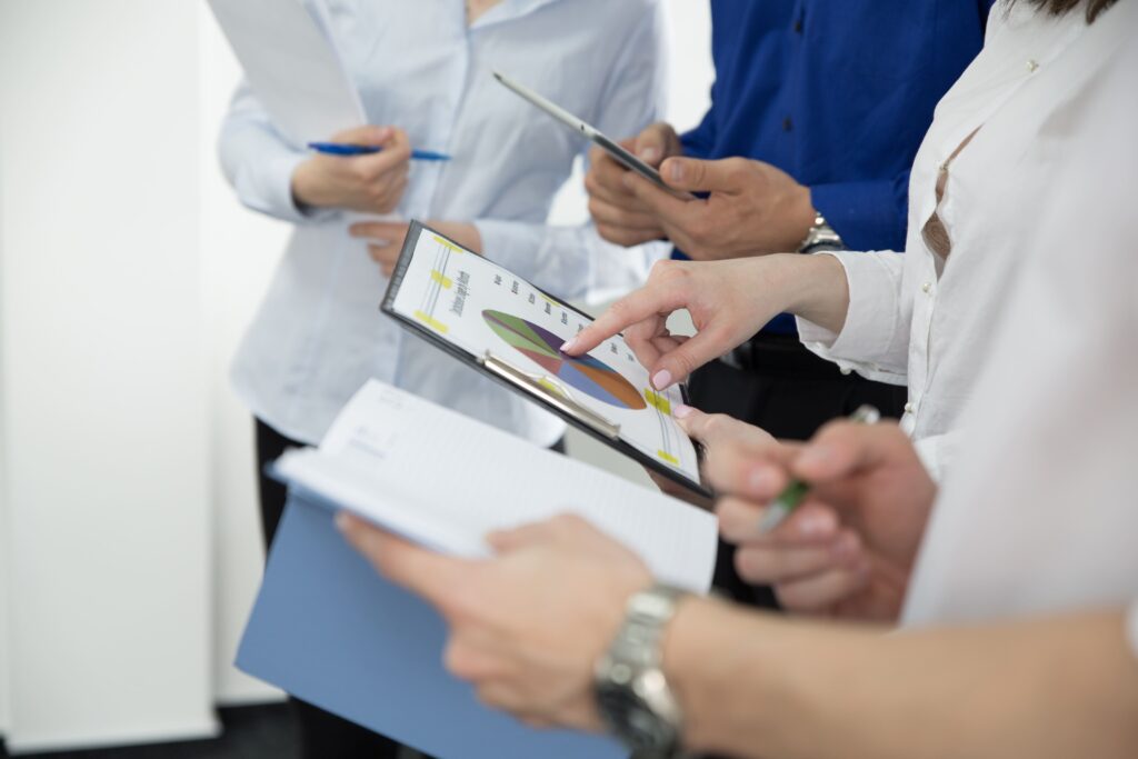 Equipe colaborando em análise de dados com gráficos e documentos, demonstrando a aplicação prática da Pesquisa Operacional em empresas. Foco na tomada de decisões estratégicas e otimização de processos através da análise de dados e informações.