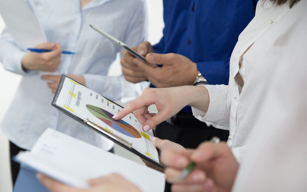 Equipe de profissionais em reunião analisando um gráfico de pizza impresso em uma prancheta, representando o planejamento prático de como aplicar a pesquisa operacional na empresa.