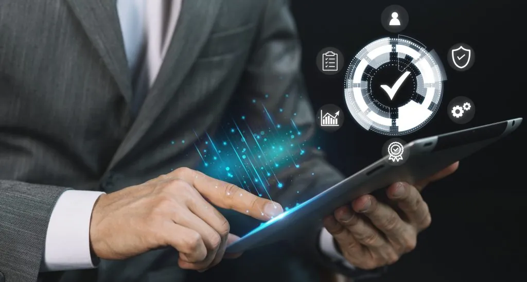 Close-up de um executivo segurando um tablet digital, de onde projetam-se hologramas gráficos, ícones de engrenagens e sinais de verificação, simbolizando a precisão e o controle tecnológico no processo de planejamento de demanda.
