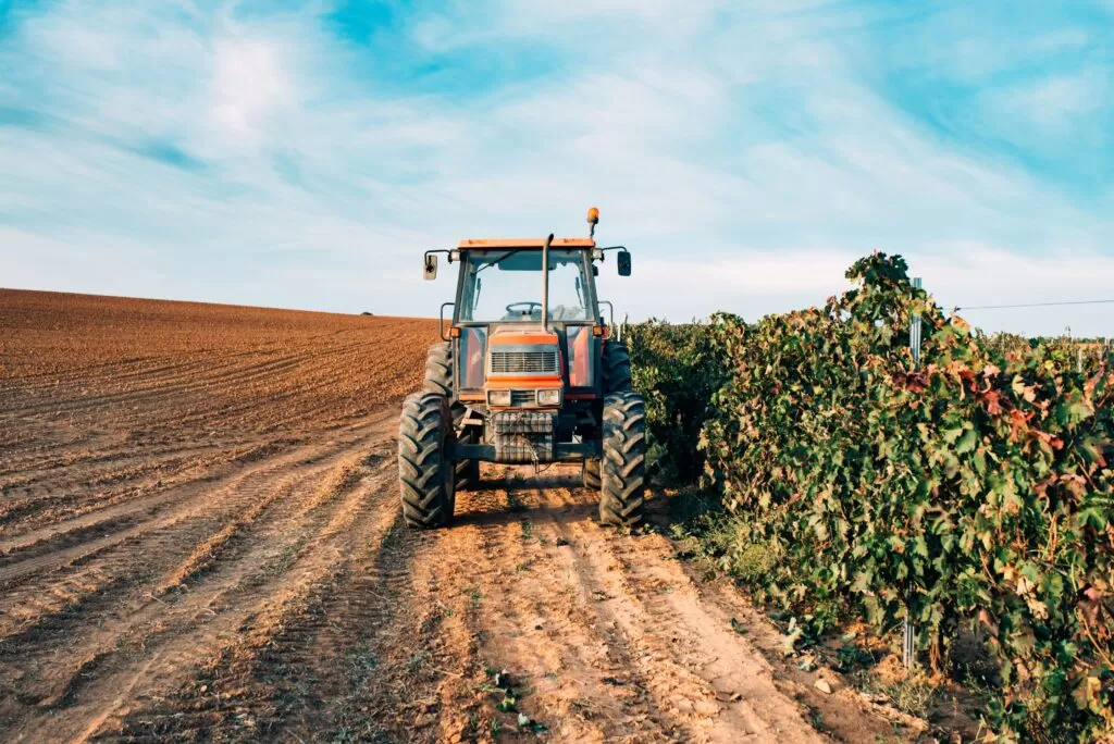 Imagem de um trator passando ao lado de uma plantação exemplificando a produção de sementes