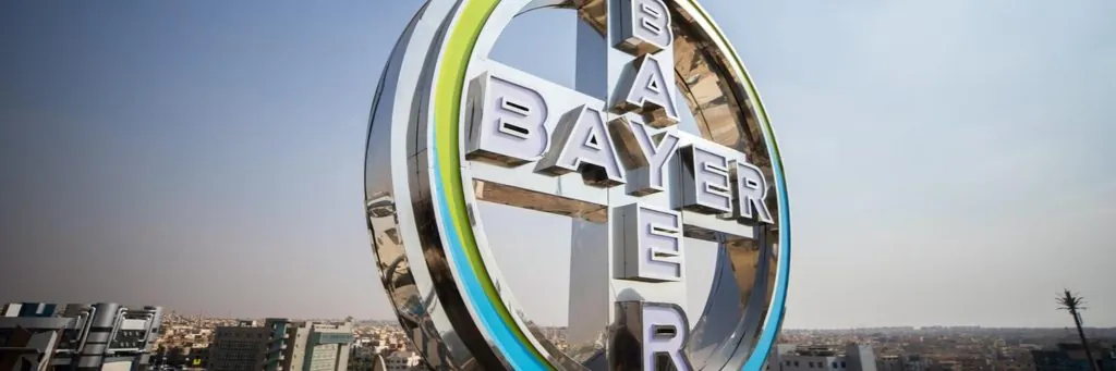 Logo da Bayer em destaque com skyline ao fundo, representando a parceria com a UniSoma Labs para planejamento de sementes.