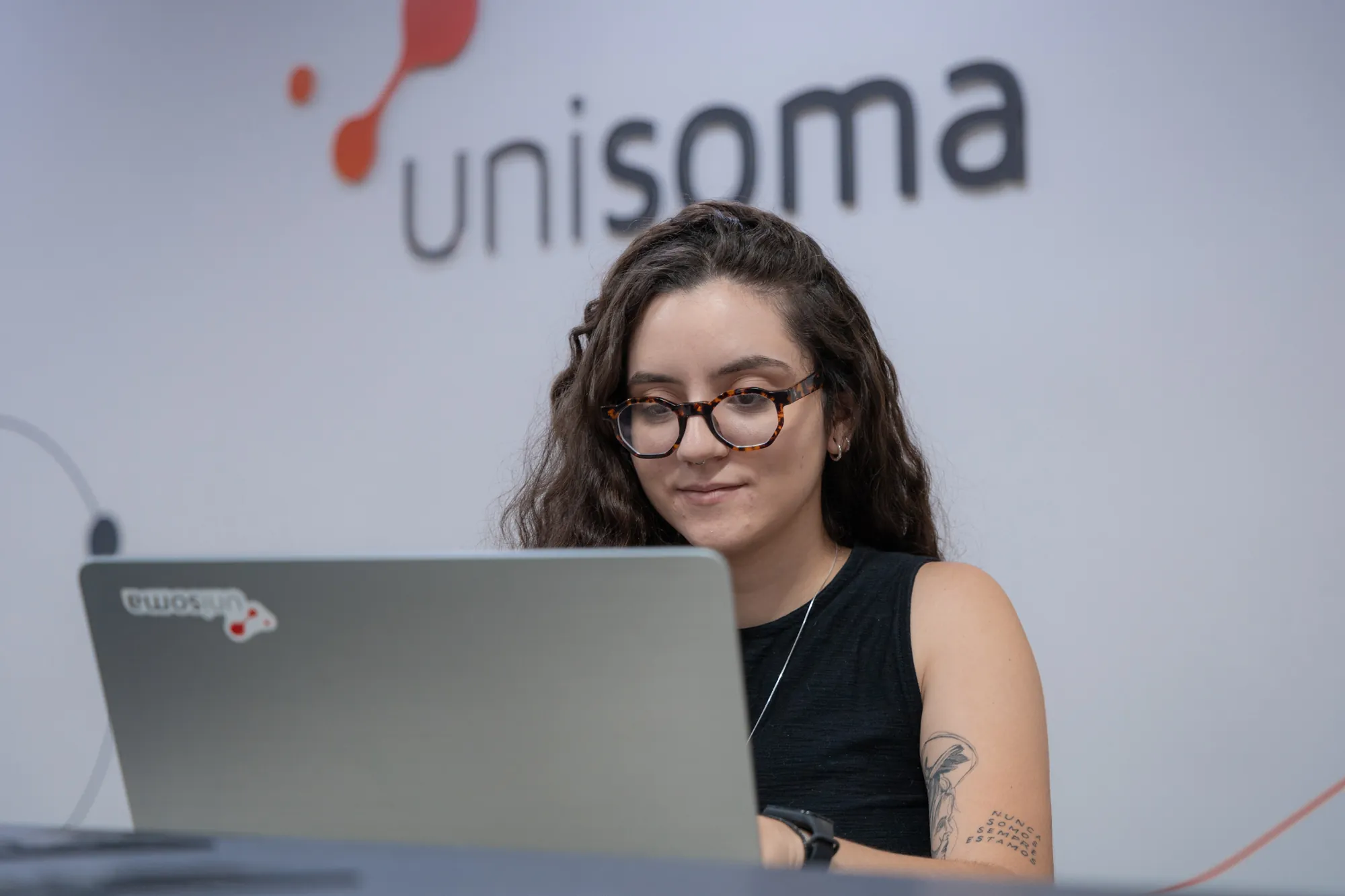 Analista da UniSoma trabalhando em laptop, com a marca da empresa ao fundo